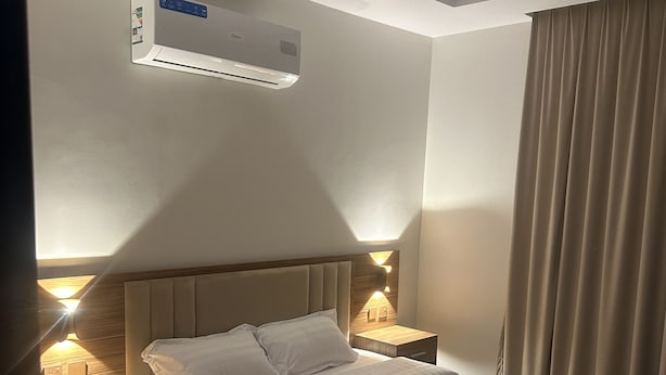 A hotel room with a large bed, two bedside tables, a wall-mounted air conditioner, and a window with curtains. - Zahrat Alandalus Apartments (Riyadh)