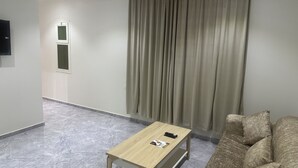A modern living room with a wooden coffee table, a beige sofa, and a large window with curtains. - Zahrat Alandalus Apartments (Riyadh)