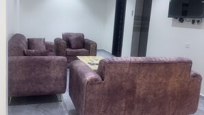 A modern living room with a sofa set, a coffee table, and a flat-screen TV mounted on the wall. - Zahrat Alandalus Apartments (Riyadh)