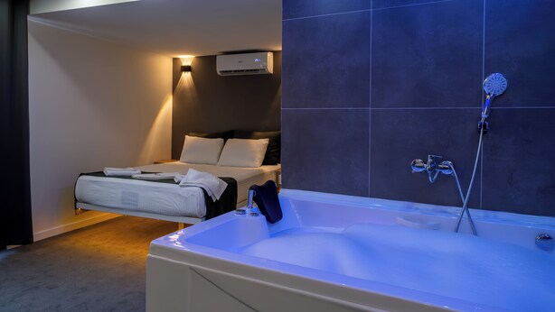 A modern hotel room with a large bathtub, a bed with white linens, and a wall-mounted air conditioner.
