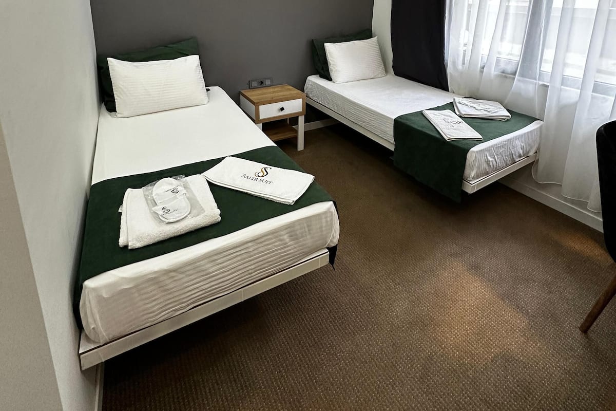 Habitación de hotel con dos camas, una mesita de noche y una ventana con cortinas.