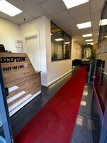 Un área de recepción con alfombra roja, un mostrador y un espejo.