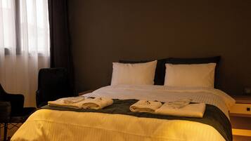 Habitación de hotel con una cama grande, una silla, un equipo de aire acondicionado y una ventana con cortinas.