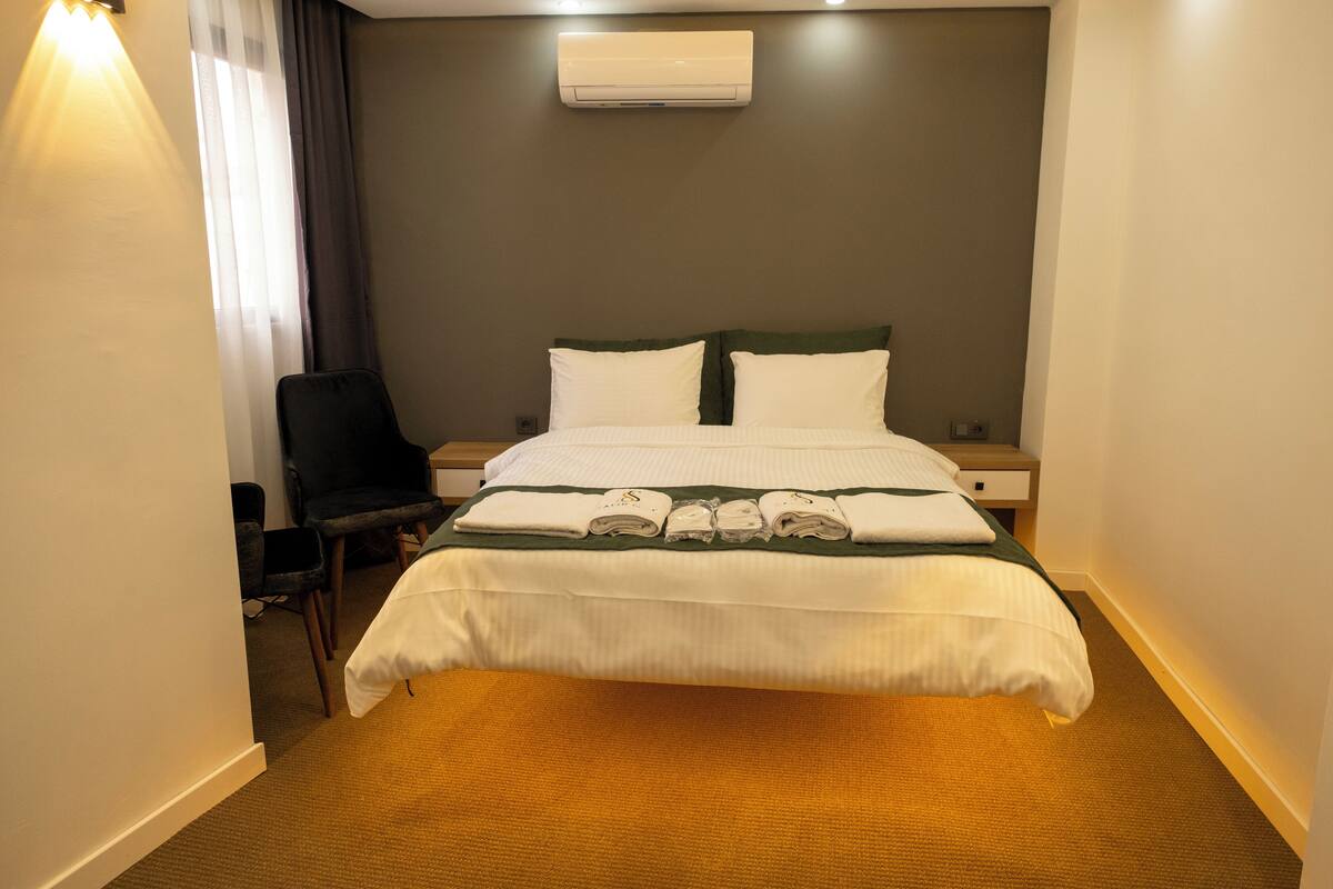 Una habitación de hotel con una cama, una silla, una mesita de noche y un aire acondicionado.