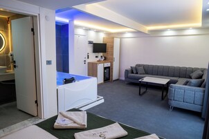 Una habitación de hotel moderna con sofá, una pequeña mesa, televisor, minibar y baño con bañera.