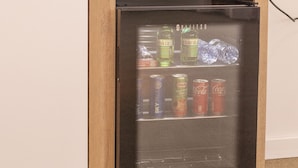 A small wooden cabinet with a built-in refrigerator containing beverages and a kettle on top.