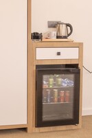 Un mueble de madera pequeño con un refrigerador incorporado que contiene bebidas y una tetera encima.