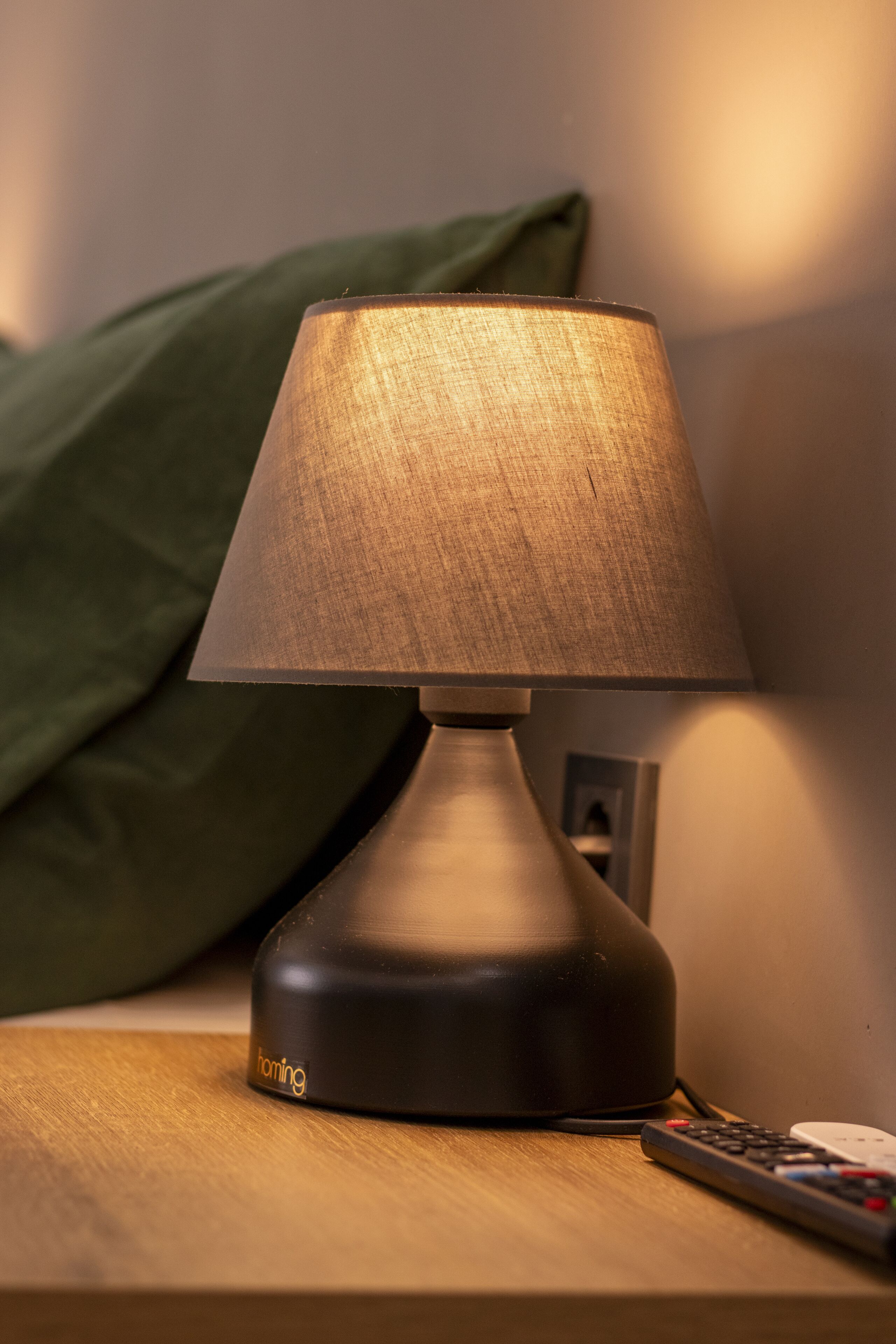 A modern lamp on a wooden bedside table with a remote control beside it.