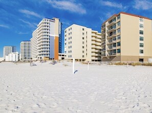 A beachfront hotel with multiple high-rise buildings, sandy beach, and clear skies.