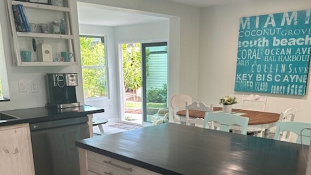 Une cuisine moderne avec un plan de travail noir, des meubles de couleur bois clair et un coin repas comprenant une table et des chaises.