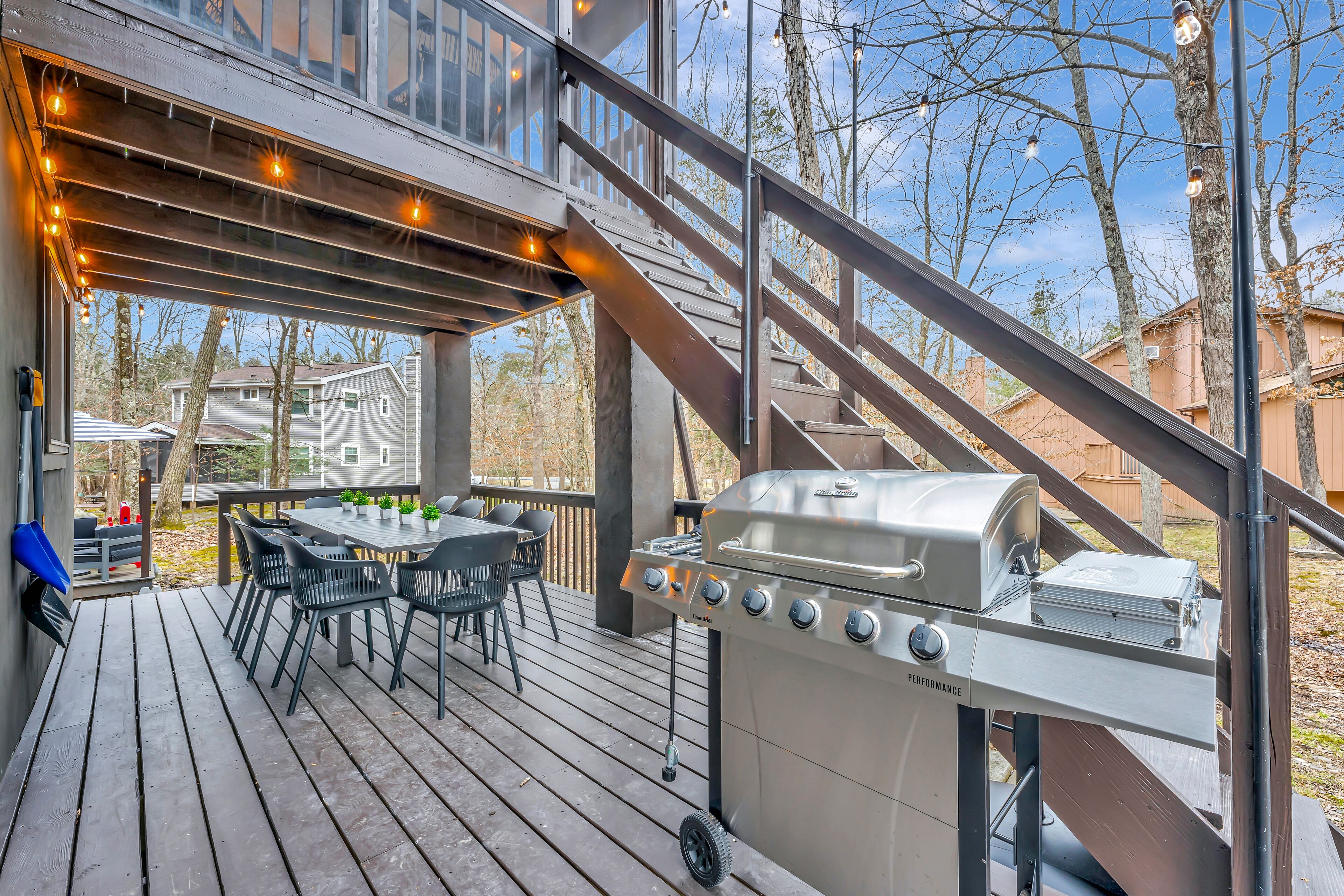 Une terrasse en bois équipée d’un barbecue, de meubles d’extérieur et d’un escalier menant à un niveau supérieur.