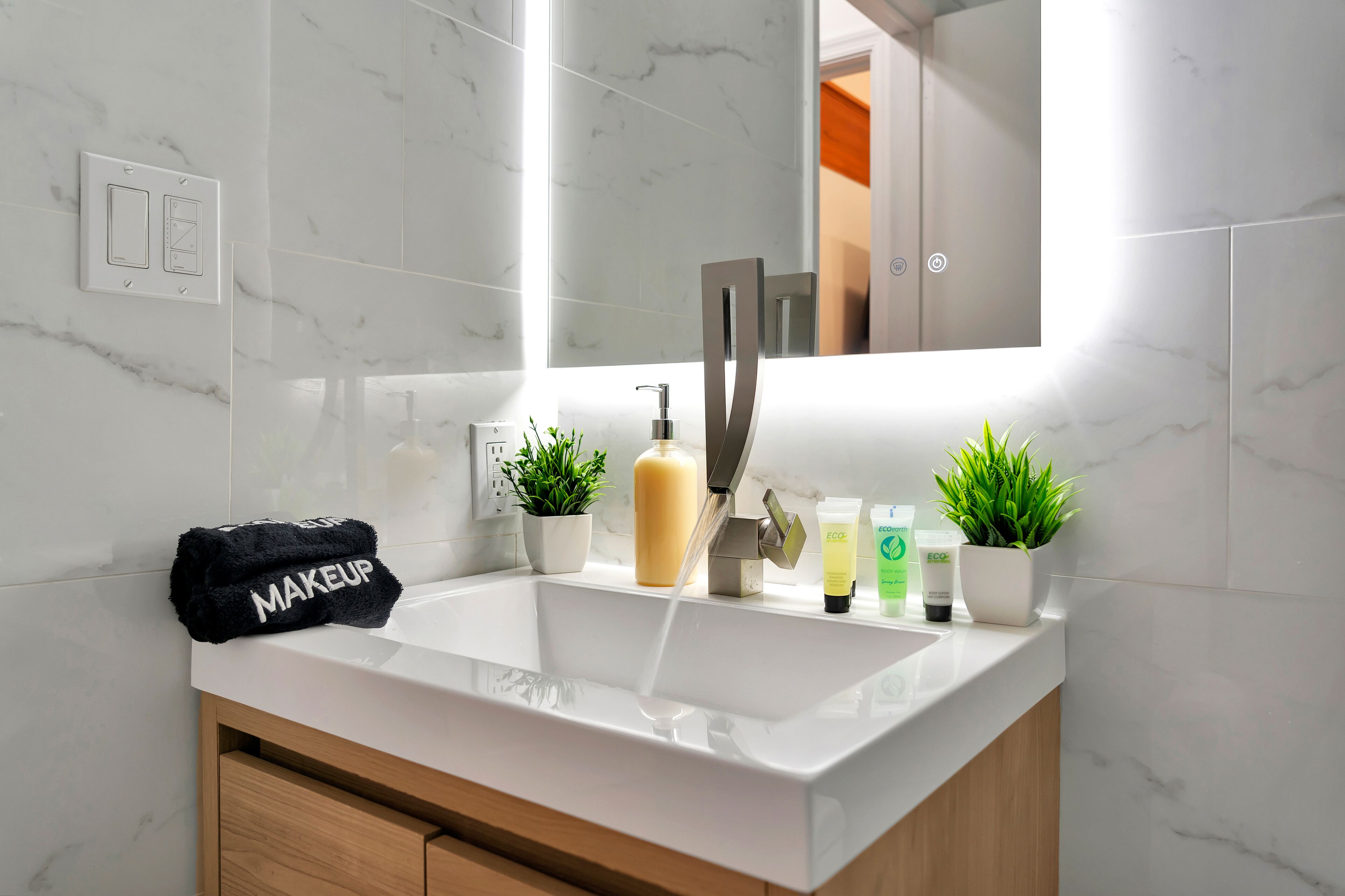 A modern bathroom with a white sink, a mirror, a towel rack, and two potted plants.