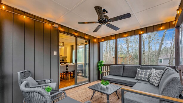 A covered outdoor seating area with a ceiling fan, wicker furniture, and a view of the house and trees. - Poconos FUN! Hot Tub, Fire Pit, Game Room, Arcade (East Stroudsburg)