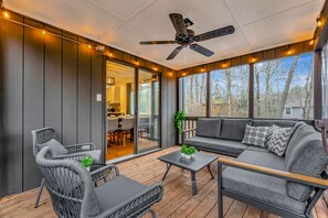 A covered outdoor seating area with a ceiling fan, wicker furniture, and a view of the house and trees. - Poconos FUN! Hot Tub, Fire Pit, Game Room, Arcade (East Stroudsburg)