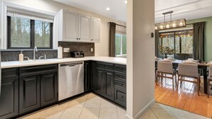 A modern kitchen with dark cabinets, a dishwasher, and a dining area with a wooden table and chairs. - Poconos FUN! Hot Tub, Fire Pit, Game Room, Arcade (East Stroudsburg)
