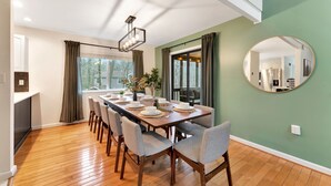 A dining room with a wooden table set for six, surrounded by six chairs, a large mirror on the wall, and a view of the kitchen through the window. - Poconos FUN! Hot Tub, Fire Pit, Game Room, Arcade (East Stroudsburg)