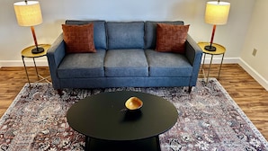 Un salon avec un canapé bleu, deux lampes, une table basse et un tapis à motifs.