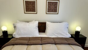 Un lit bien fait, avec une couette marron, deux oreillers blancs et deux tables de chevet dotées de lampes.