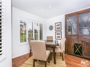 A dining area with a wooden table and chairs, white walls, and a wooden cabinet with glass doors.