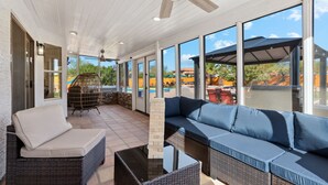 Un patio cubierto con mobiliario de mimbre, un separador de vidrio y vistas a una piscina y edificios.