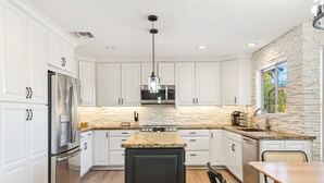 Una cocina moderna con armarios blancos, encimera de granito, electrodomésticos de acero inoxidable y una pared de detalles de piedra.