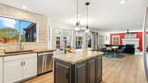 Una cocina moderna con una isla grande, electrodomésticos integrados y una zona de comedor con una pared de acento roja.
