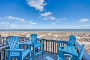 Terraza de madera con sillas Adirondack azules que dan a la playa.