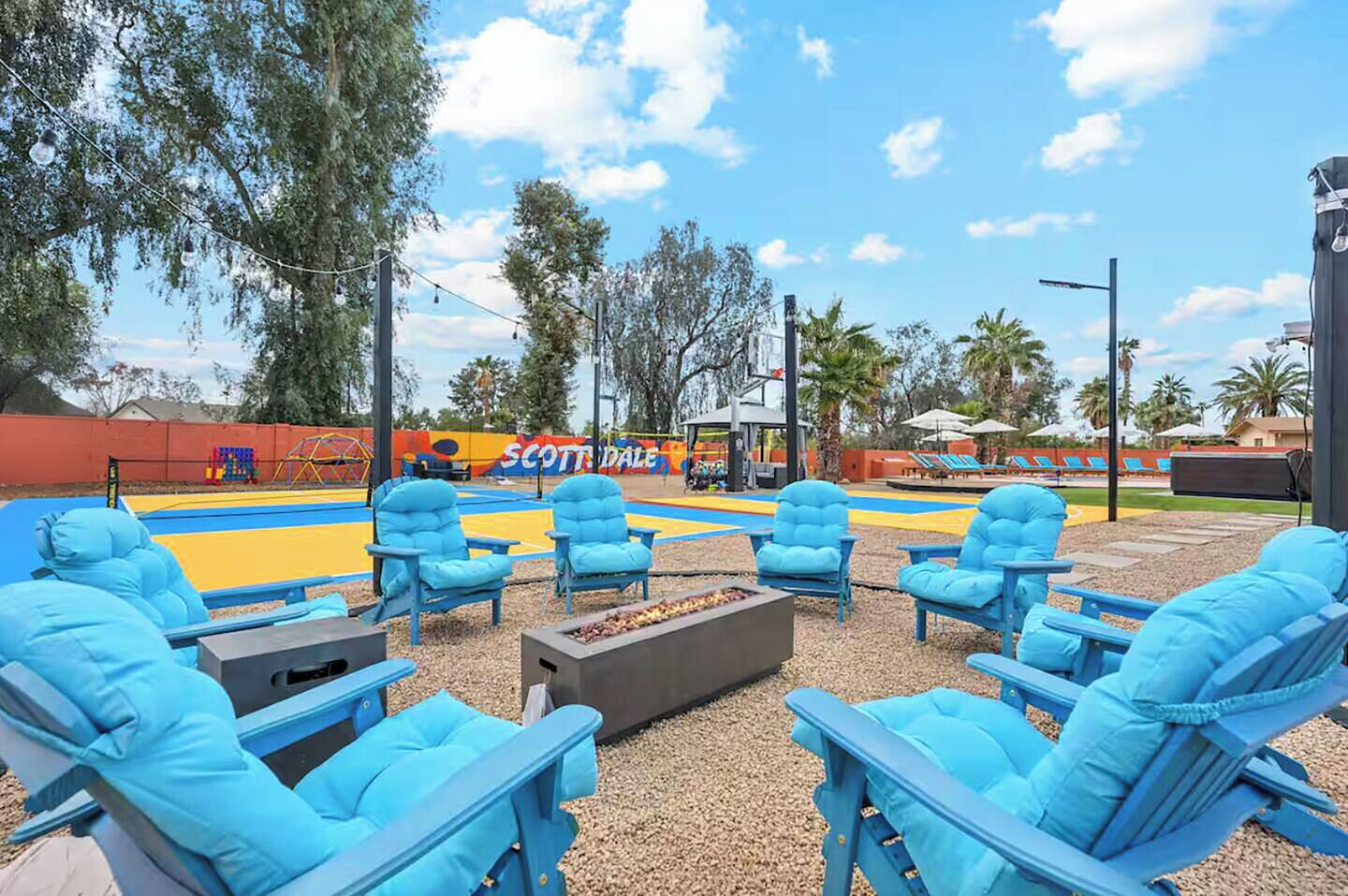 Ein Außenbereich mit blauen Stühlen und einem Feuerkorb, umgeben von einem Spielplatz und einem Poolbereich.