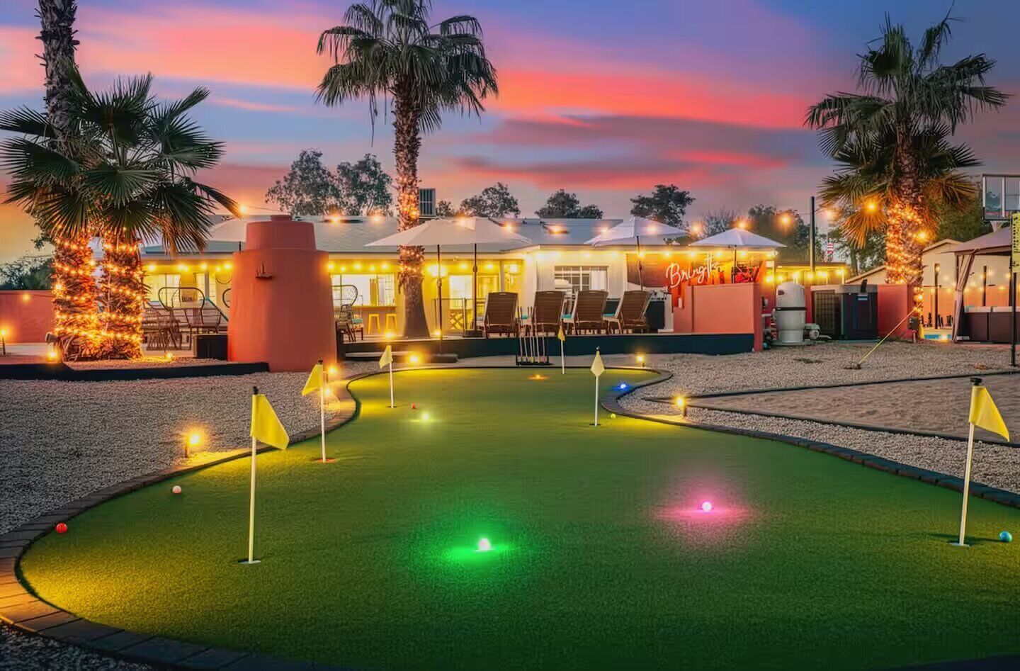 Ein Golfplatz mit Putting Green, umgeben von Palmen und einem Gebäude mit Außenplätzen.