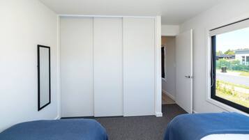 Ein Hotelzimmer mit zwei Betten, einem Kleiderschrank, einem gerahmten Bild und einem Fenster mit Blick nach draußen.