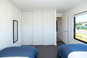 A hotel room with two beds, a wardrobe, a framed picture, and a window with a view of the outside. - Vinebox on Wilson, Martinborough (Martinborough)