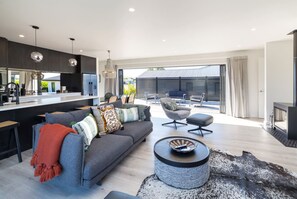 A modern living room with a sofa, ottoman, and a round coffee table. There is a dining area with a kitchen in the background. - Vinebox on Wilson, Martinborough (Martinborough)