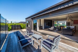 A modern outdoor living area with a wooden deck, seating, and a glass door leading to an interior space. - Vinebox on Wilson, Martinborough (Martinborough)