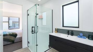 Een moderne badkamer met een glazen douchecabine, een grote spiegel en een witte wastafel met zwarte kastjes.