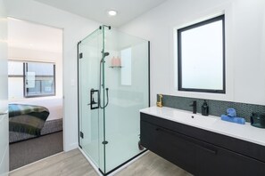 A modern bathroom with a glass shower enclosure, a large mirror, and a white vanity with black cabinets. - Vinebox on Wilson, Martinborough (Martinborough)