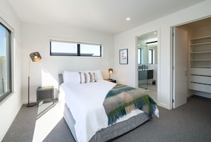 A modern bedroom with a large bed, bedside lamps, a wardrobe, and a view of the outside.