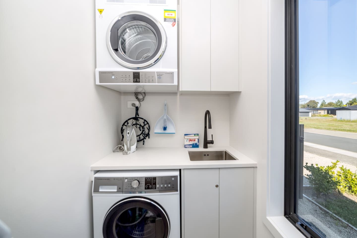 Une petite buanderie équipée d’un lave-linge à chargement frontal, d’un sèche-linge et d’un évier avec un robinet.