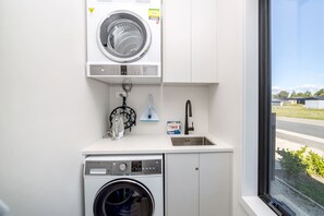 A compact laundry room with a front-loading washing machine, a dryer, and a sink with a faucet. - Vinebox on Wilson, Martinborough (Martinborough)