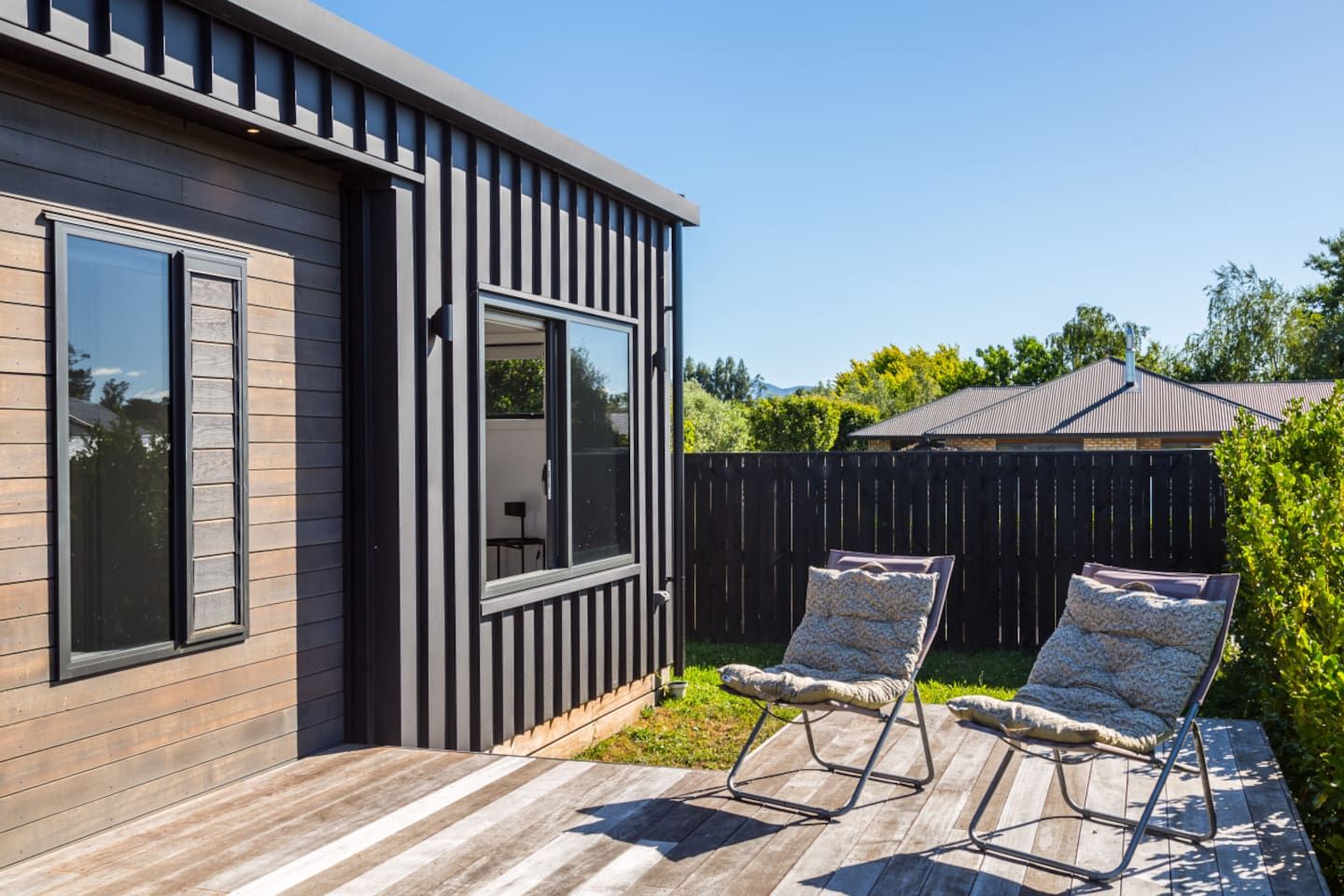 A modern house with a wooden deck, two lounge chairs, and a fenced backyard.