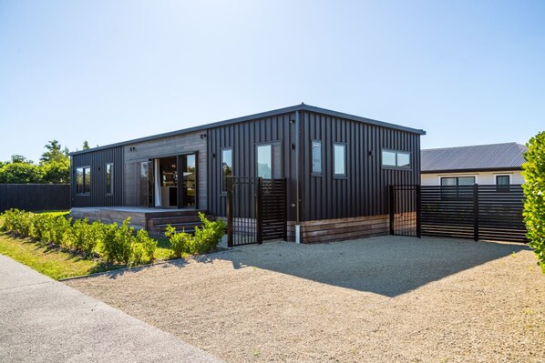 A modern building with a gravel driveway, a black gate, and a small garden area.