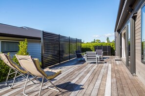 A wooden deck with outdoor furniture, a privacy fence, and a building with large windows. - Vinebox on Wilson, Martinborough (Martinborough)