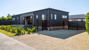 A modern, single-story building with a metal exterior, a gravel driveway, and a black gate. - Vinebox On Wilson, Martinborough (Martinborough)