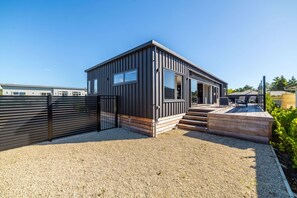 A modern, single-story building with a gravel driveway, a wooden deck, and a black metal gate. - Vinebox on Wilson, Martinborough (Martinborough)