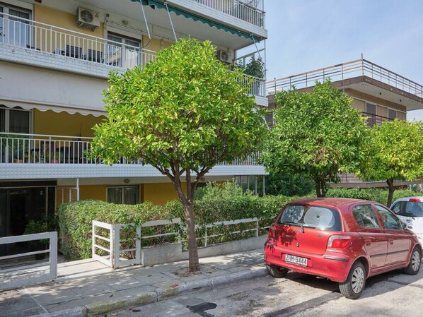 A red car parked on a street in front of a building with balconies and a tree in the foreground. - Elegant Boutique Apt in Kifissia (Kifisia)