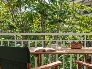 A wooden table with an open book, a glass of water, and a potted plant on a balcony with a white railing. - Elegant Boutique Apt in Kifissia (Kifisia)