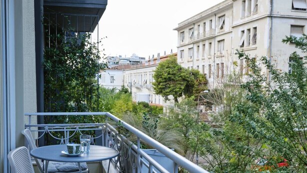 Ein Balkon mit Tisch und Stühlen, umgeben von Grünpflanzen und Blick auf eine Stadtlandschaft.