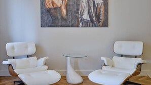 Ein Zimmer mit zwei weißen Ledersesseln, einem kleinen Glastisch und einem Gemälde an der Wand.