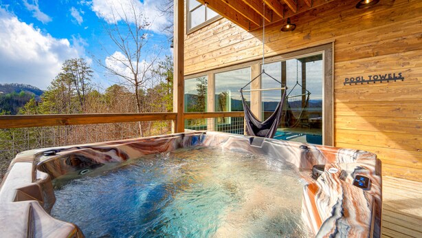 A wooden cabin with a hot tub, large windows, and a view of the mountains.