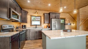 A modern kitchen with dark cabinets, stainless steel appliances, and a large island.