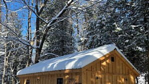 Una cabaña de madera con techo cubierto de nieve, rodeada de árboles.